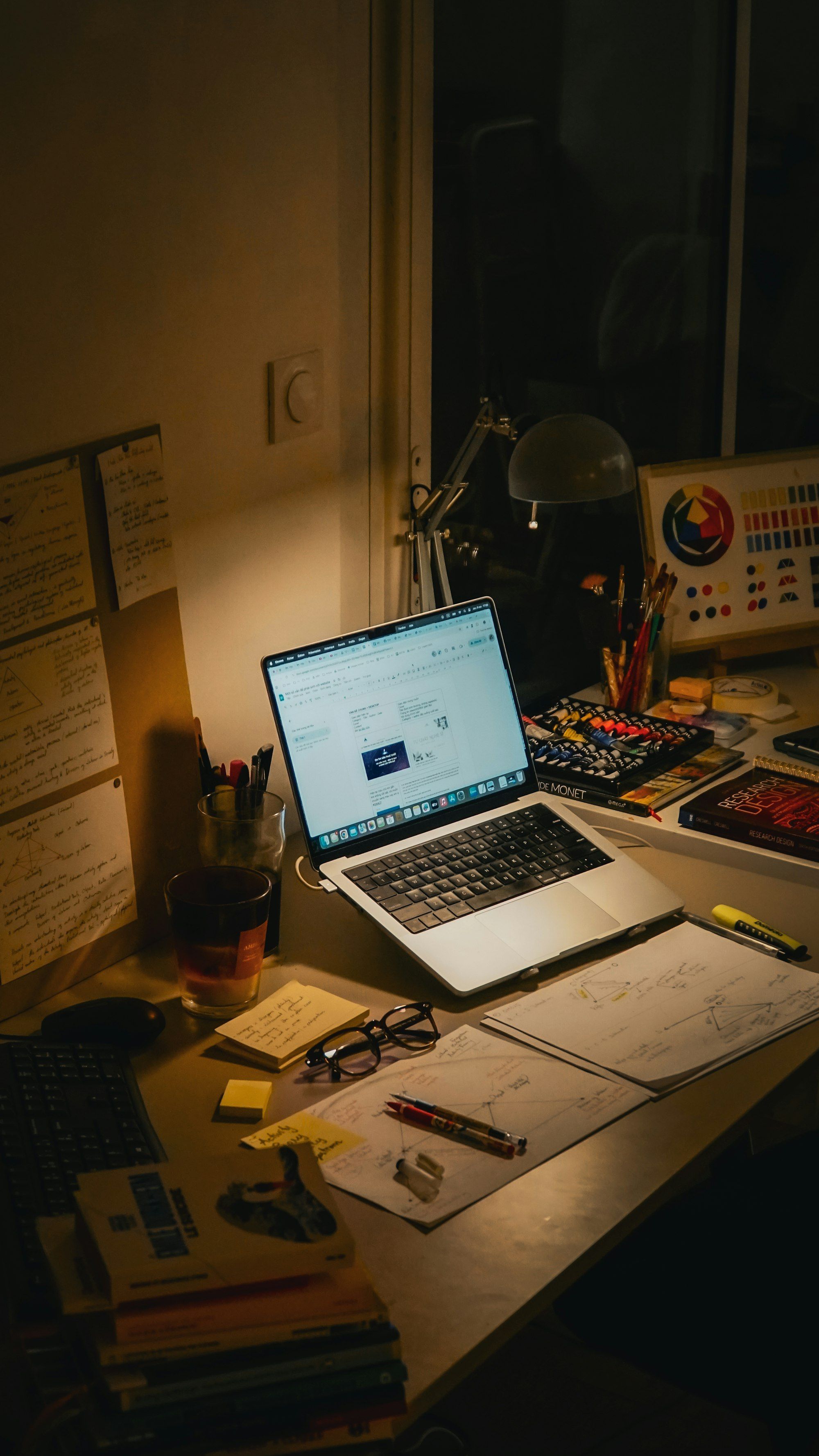 Desk at night with an open laptop, notebooks and papers under a lamp